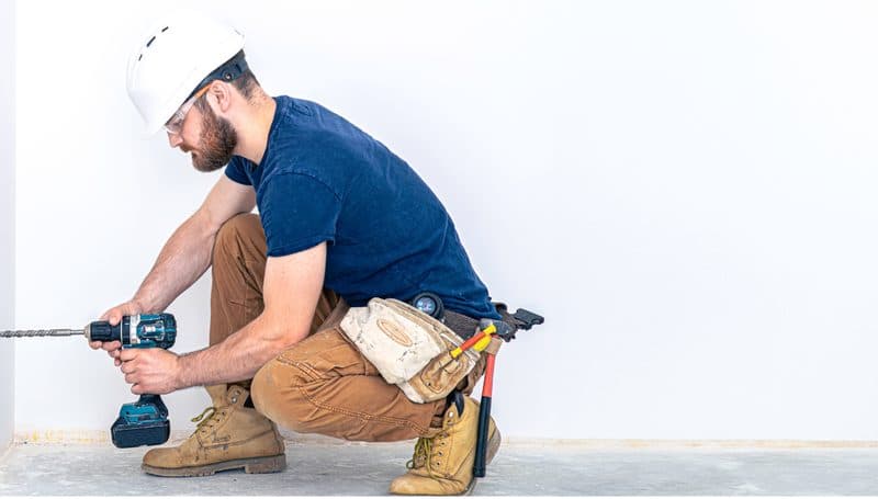 Tradesperson kneeling with a cordless drill